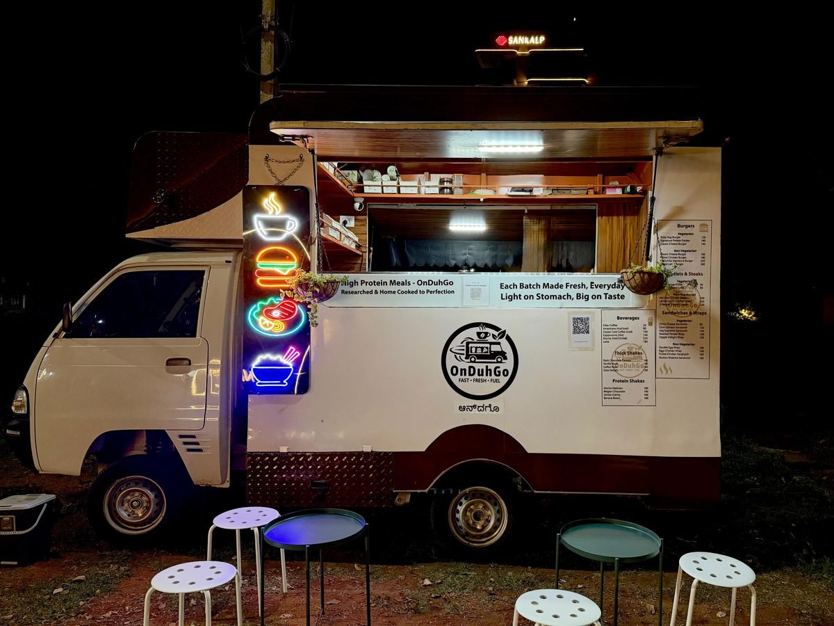 The OnDuhGo truck after dark, hatch up and the neon food signs lit, with stools and tables set out in front